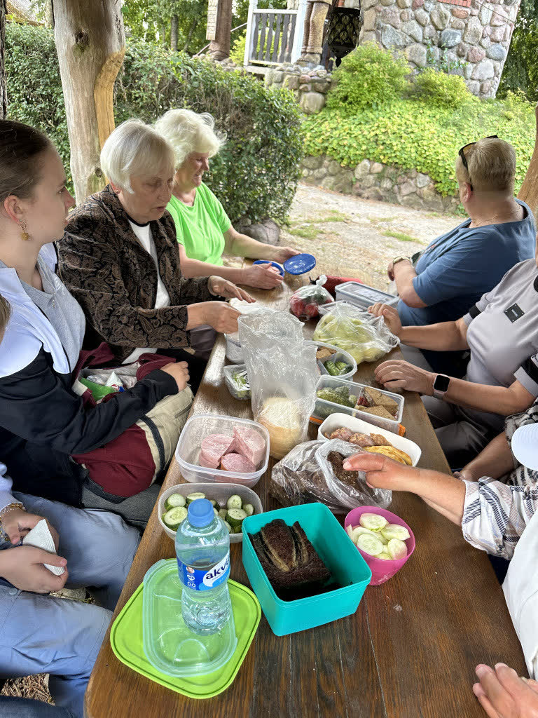 Dalyviai prie ilgo stalo pavėsinėje per edukacinį užsiėmimą